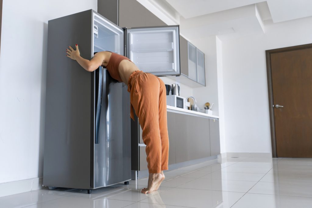 On a hot day, a girl cools down with her head in the refrigerator. Her air conditioning system is in need of repair.