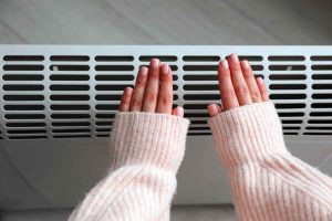 Woman warming hands near electric heater system at home