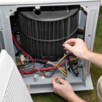 A heat pump maintenance technician working on a unit at Lake of the Ozarks